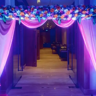 An inviting entrance arch we designed for an evening event. It features a lush floral arrangement on top with draped pink fabric, all highlighted by vibrant purple and pink event lighting.