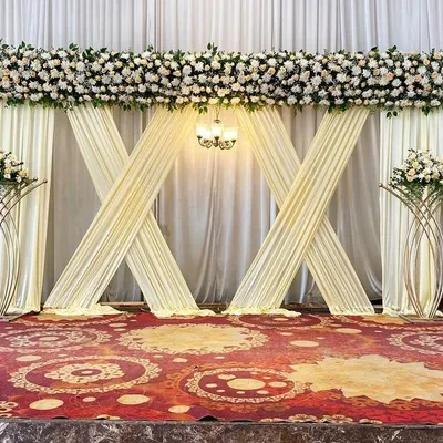 This modern stage for a Beegara Oota features criss-cross white drapes, classic floral arrangements, and a central chandelier for a sophisticated look.