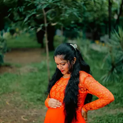 A quiet moment of connection in a peaceful park setting. This outdoor maternity portrait captures the mother-to-be in a vibrant orange dress, surrounded by natural greenery.