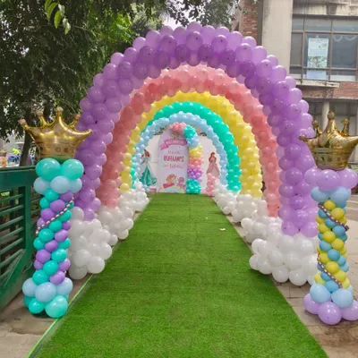 A spectacular rainbow balloon arch creating a magical tunnel entrance for a princess party on a green lawn.