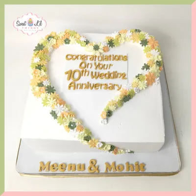 A decade of love celebrated with a beautiful heart-shaped cake. This design features a wreath of delicate, hand-piped flowers in soft green and yellow hues, perfect for a 10th wedding anniversary.