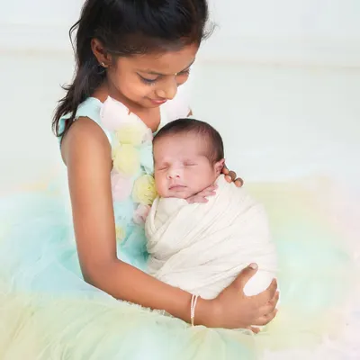 A big sister looks down with so much love at her sleeping newborn sibling. The pastel colors of her dress add a soft, dreamy feel to this incredibly sweet moment.