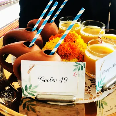I love serving drinks in creative ways. Here, our 'Cooler 49' orange drink is presented in traditional clay 'surahis' alongside regular glasses, garnished with marigold flowers for a festive look.