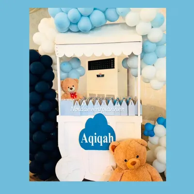 We design custom carts that fit your event's theme perfectly. This white cart, decorated with blue balloons and teddy bears for an Aqiqah, is a beautiful way to display favors, desserts, or welcome drinks for your guests.