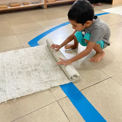 The day begins with choosing a workspace. A child carefully unrolls his mat, an important Montessori exercise that defines his personal area and teaches respect for his own work and the work of others.