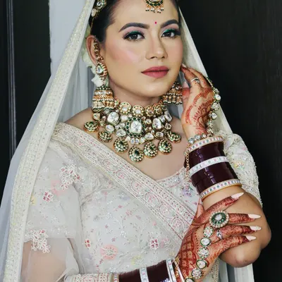 A stunning modern bride in a white lehenga. The makeup features a pop of green eyeliner, soft pink tones, and a flawless base, complemented by heavy Kundan jewellery.
