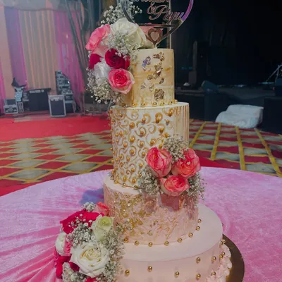 A four-tiered masterpiece fit for a royal celebration. This cake combines different textures, from smooth pink buttercream to intricate gold piping, all brought together with cascades of fresh pink and white roses.