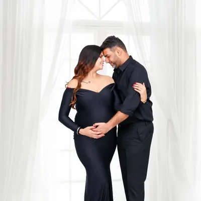 An intimate studio portrait of an expecting couple sharing a quiet moment, their foreheads touching. The soft lighting and their coordinated black outfits create a feeling of timeless elegance and deep connection.
