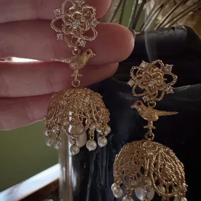 A close up of my handcrafted jhumka earrings. The design features a delicate bird motif and intricate filigree work in 18k gold, creating a classic dome shape adorned with pearls and diamonds.