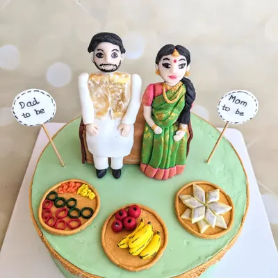 This traditional baby shower cake was a joy to create. It features handcrafted fondant toppers of the parents-to-be, along with miniature plates of traditional sweets and fruits.