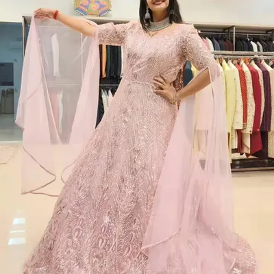 A full view of the stunning pink embroidered gown, showing its beautiful flare and the way the light catches the sequins. The attached cape-like sleeves add a touch of drama.