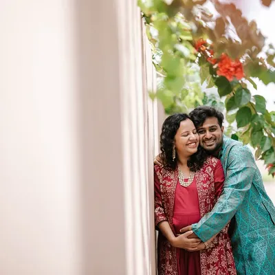An expecting couple shares a happy, intimate moment during their outdoor maternity shoot. The natural frame of flowers and sunlight adds a warm, romantic touch to this candid portrait.