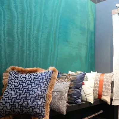 A row of our exquisite cushions, featuring a variety of textures from intricate beading to plush fur trim, set against a vibrant turquoise wallcovering. This showcases how our fabrics and wallpapers can be coordinated to create a rich, layered look.