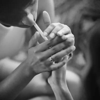 An intimate black and white close-up of two people sharing a moment, with one lighting a cigarette for the other. The focus on their hands creates a raw and personal narrative.