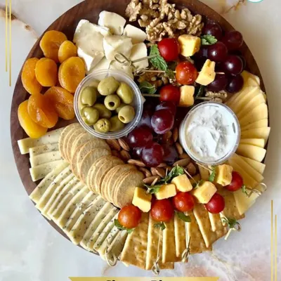 My signature vegetarian Cheese Platter. This artfully arranged board includes a selection of cheeses, crackers, nuts, dried and fresh fruits, and olives. It's a feast of textures and flavors.