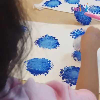 A child uses bubble wrap to create beautiful blue hydrangea blossom prints. This tactile art activity is a fun and creative way to explore textures and patterns.
