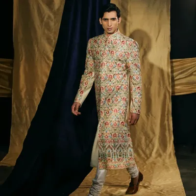 A kingly statement. This cotton silk sherwani is fully adorned with intricate multi-color Resham work, creating a wearable piece of art for your wedding day.