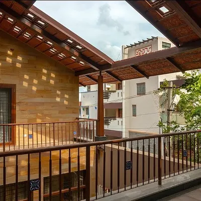 The upper-level veranda at Nivriti, Chatty’s House, overlooks a central open space, creating connectivity between different parts of the home. The perforated roof design allows dappled sunlight to filter through, creating dynamic light patterns.