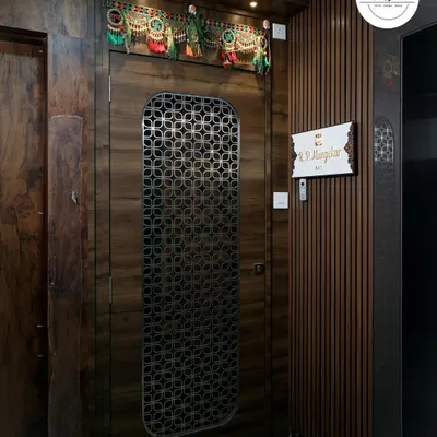A statement entrance featuring a main door with a custom geometric metal grill. The surrounding wall is clad in dark wood paneling, creating a rich and sophisticated welcome.