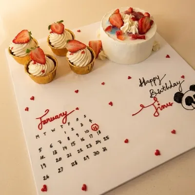 A truly personal birthday gift. This custom creation features a hand-piped calendar marking the special day, alongside a mini cake and fresh strawberry cupcakes.