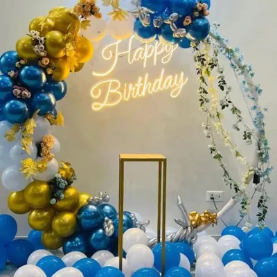 A classic and clean balloon arch design perfect for any celebration. This setup features a mix of blue, gold, and white balloons, with a warm 'Happy Birthday' neon sign at the center. It's a versatile backdrop that works well in many spaces.