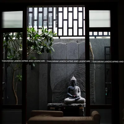 A view from indoors looking out into a tranquil courtyard we designed. A meditative Buddha statue sits as the centerpiece, framed by glass doors and complemented by a single tree, creating a perfect picture of serenity.