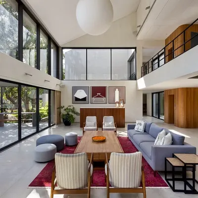 The living area of the Mango Orchard House is a study in volume and light. The double-height ceiling and expansive glass walls create a powerful connection to the outdoors, while the furniture arrangement fosters intimate conversation zones within the grand space.