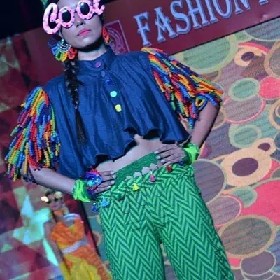 A standout piece from a student fashion show. This outfit showcases imaginative design, combining a structured denim top with playful, multi-colored tassels and vibrant patterned trousers, demonstrating a strong, modern aesthetic.