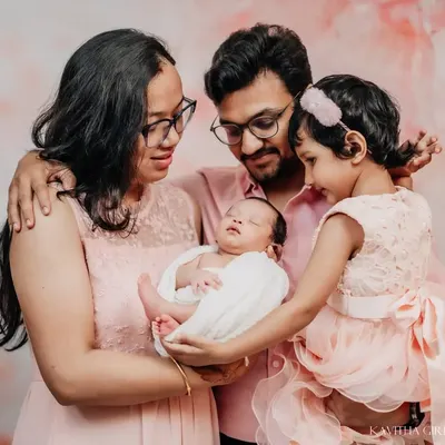 A beautiful first portrait as a family of four. The parents and big sister gaze lovingly at the newest member, all coordinated in soft pink tones for a warm and cohesive family photo.