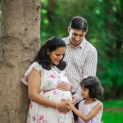 A heartwarming family moment where the older sister gently touches her mother's baby bump, with the father looking on lovingly.