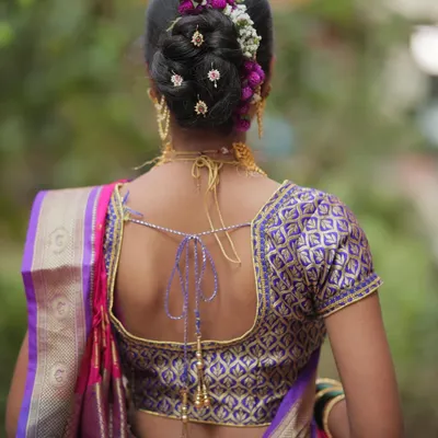 A detailed look at a traditional Maharashtrian Khopa hairstyle. The bun is decorated with fresh flowers and gold accessories, which is a classic choice for brides.