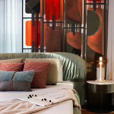 A closer look at the master bedroom's details, including the plush, layered pillows and the elegant side table. The sculptural headboard, with its mix of colors and textures, serves as a stunning piece of art.
