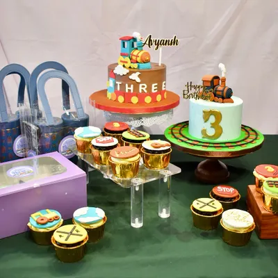 All aboard for a spectacular 3rd birthday. This train-themed dessert table features two custom cakes, dozens of themed cupcakes, and party hampers, creating a complete and cohesive celebration spread.