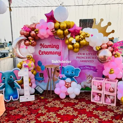 A royal welcome for a little princess. This naming ceremony on a rooftop features a large storybook-style backdrop, a pink, gold, and white balloon arch, and cute elephant cutouts.