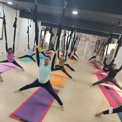 A full class of students exploring aerial yoga, using the hammocks to stretch and strengthen in unison. This is a great way to build community and have fun.