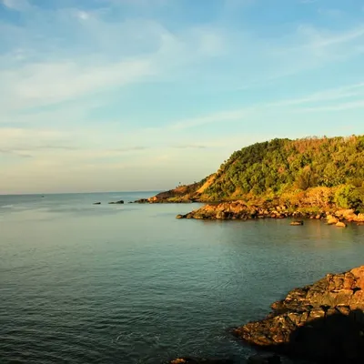 The beautiful coastline of Gokarna at golden hour, showing the rocky shores and green hills that we trek along.