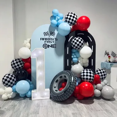 A "Aarav's Fast One" race car themed first birthday. This dynamic setup features a racetrack backdrop, checkered flag balloons, a large light-up number '1', and an inflatable tire prop for a high-energy celebration.