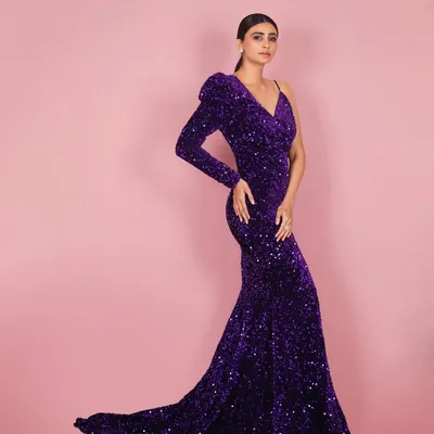 A full-length shot of actress Daisy Shah in a magnificent purple sequined gown. The one-shoulder design and flowing train are captured with studio lighting to emphasize the drama and elegance of the outfit.