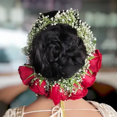 A classic bridal bun, beautifully decorated with a circle of fresh red roses and baby's breath. This is a timeless choice for any wedding ceremony.