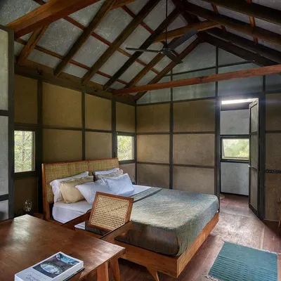 The bedroom of the prefab earthen prototype cottage. The design uses a simple palette of wattle-and-daub walls, a wooden frame, and an exposed timber roof to create a warm, serene, and rustic space.