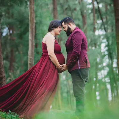 An intimate portrait of an expecting couple in a beautiful forest setting. The flowing red gown adds a touch of drama and elegance to the natural surroundings.