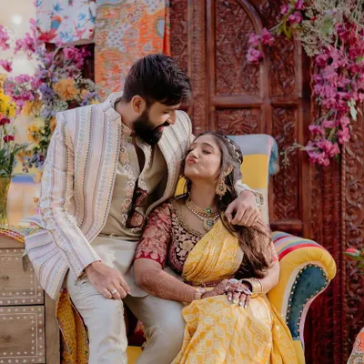 A candid moment of the happy couple at their 'Rajasthani Folklore' Mehendi. The colorful patchwork chair and floral backdrop created a picture-perfect setting.