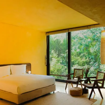 The main bedroom of the Banyan Suite, where minimalist design and natural materials create a calming atmosphere, with the entire wall opening up to a view of the forest.