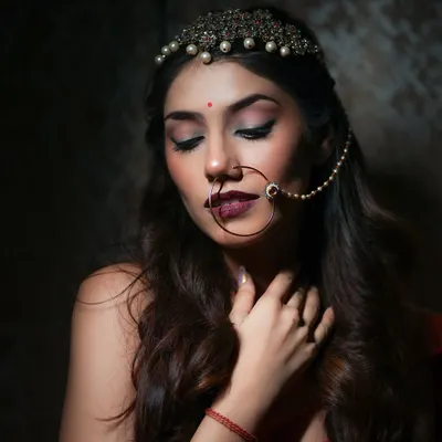 An elegant close-up from an Indian bridal-style shoot. The focus is on the intricate jewelry, like the nath and matha patti, and the soft, expressive makeup, creating a timeless and beautiful portrait.