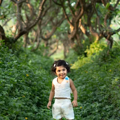 A beautiful portrait of a toddler standing in a field of lush green clover. The winding path of trees creates a magical, forest-like setting.