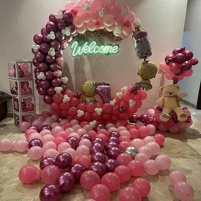 A beautiful crescent moon balloon structure for a baby girl's welcome. The setup includes a "Welcome" neon sign, teddy bears, and a sea of pink and magenta balloons on the floor for a dreamy effect.