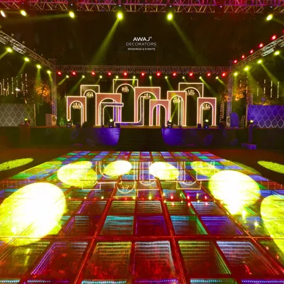 A high-energy Sangeet stage with a multi-level, LED-lit backdrop and a reflective dance floor, ready for a night of performances.