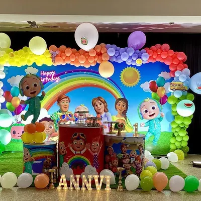A bright and cheerful Cocomelon themed birthday party. This wide shot shows the complete setup with a large character backdrop, a rainbow balloon arch, themed pedestals, and character cutouts, perfect for fans of the popular show.