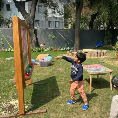 Our outdoor space becomes a large-scale art studio. Here, a child throws a paint-soaked ball at a clear easel, learning about trajectory, force, and color mixing in a dynamic, full-body engagement.