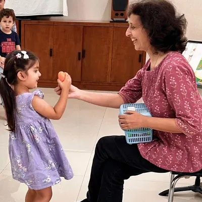 A teacher shares a shaker egg with a young student. This simple interaction is a foundational step in introducing rhythm and sound exploration in a gentle, one-on-one setting.